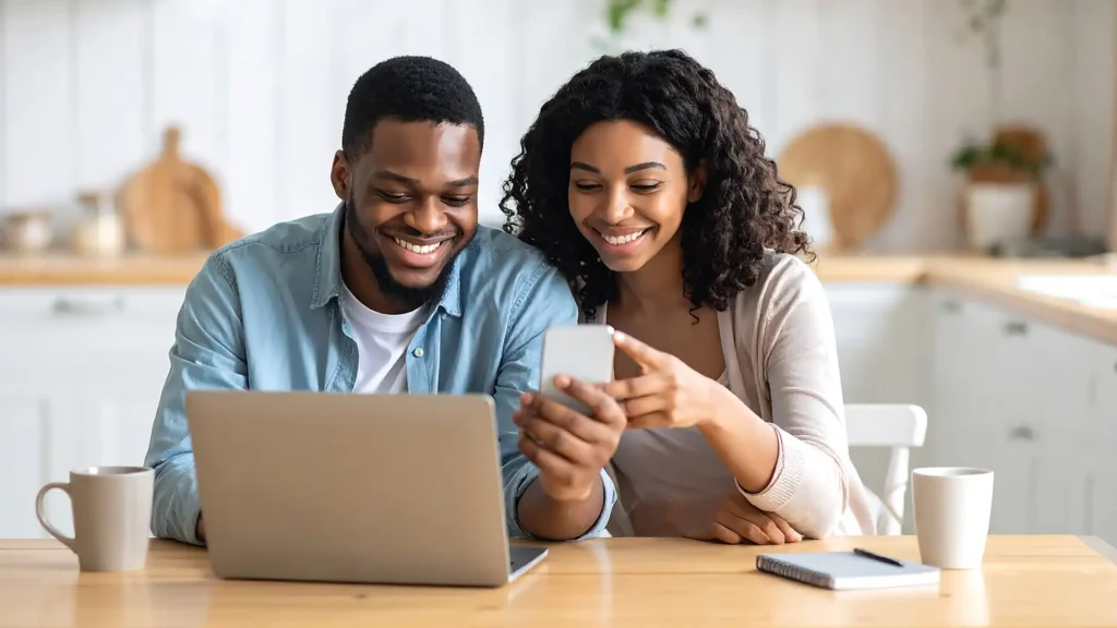 Happy couple on their laptop and smartphone in a kitchen
