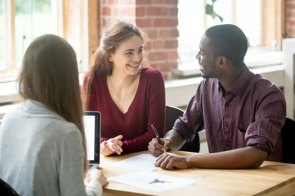 Happy couple looking at each other before signing contract in front of female real estate agent.