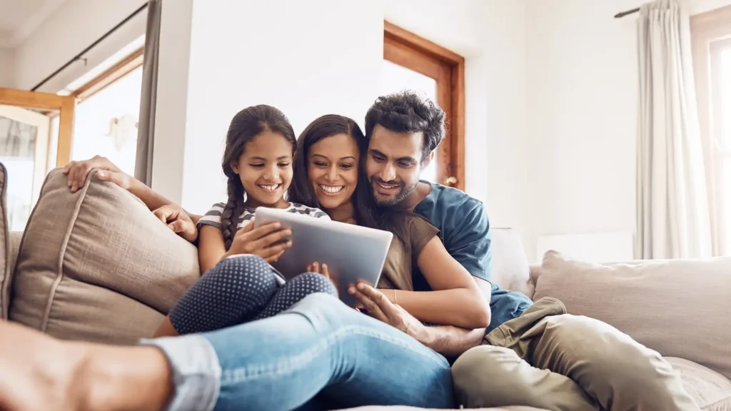 Mother, father, and young girl use a digital tablet together on the sofa at home